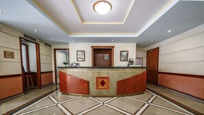 Ein Hotel-Empfangsbereich mit einer zentralen Rezeption, gerahmten Kunstwerken an den Wänden und einem gefliesten Boden.