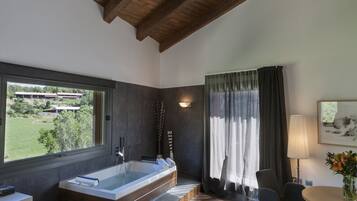 A modern bathroom with a large bathtub, a window with a view of greenery, and a wooden ceiling.