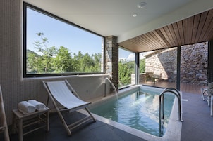 Piscina interior moderna con vistas despejadas a la vegetación exterior, paredes de piedra y techo de madera.