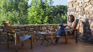 Una persona relajándose en una terraza de madera, con un muro de piedra y follaje al fondo.