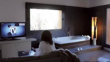 Una sala de estar moderna con un ventanal grande, un televisor de pantalla plana, un sofá, una mesita y una bañera.