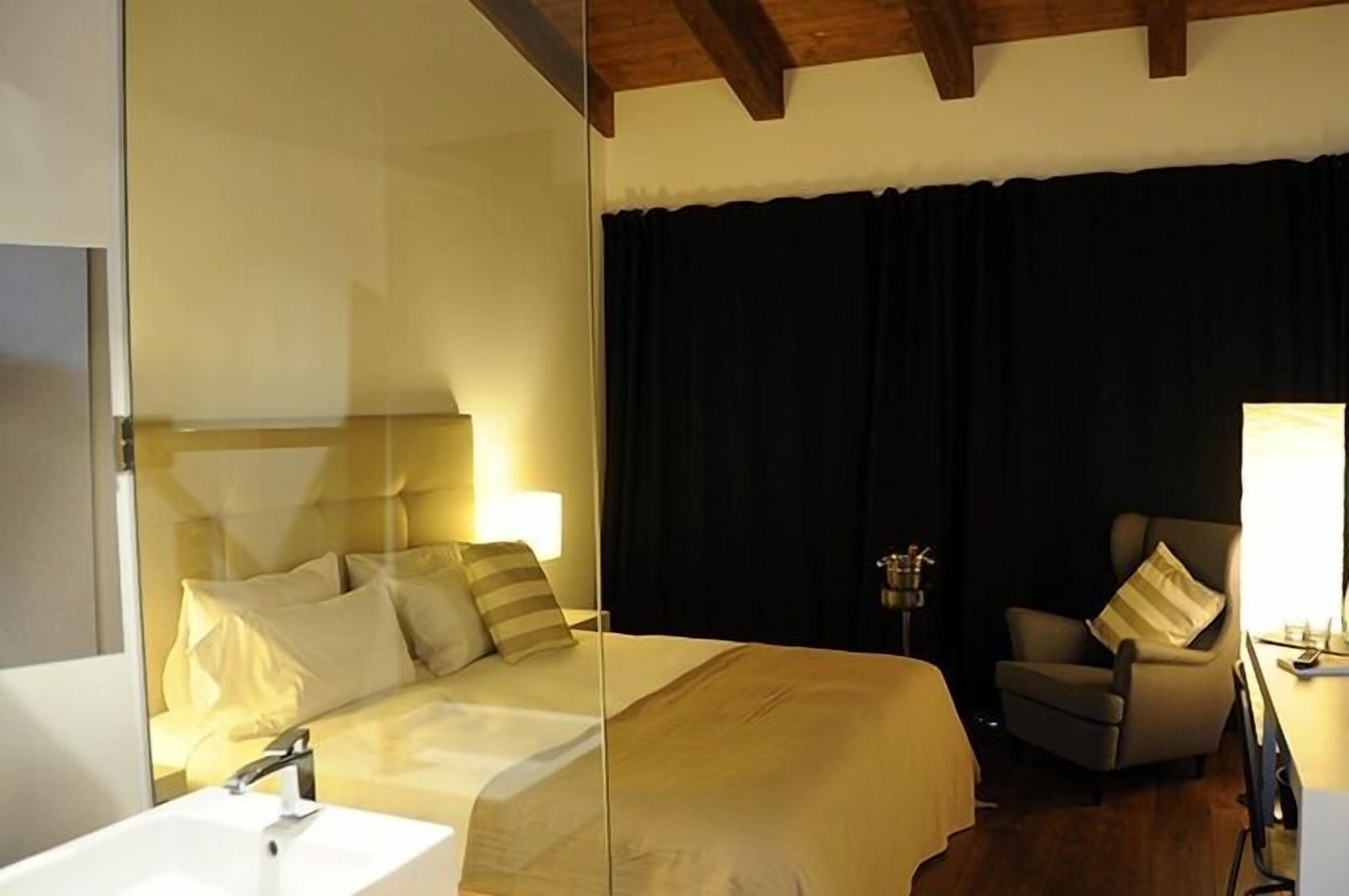 A hotel room with a bed, a chair, a desk, a lamp, and a mirror.