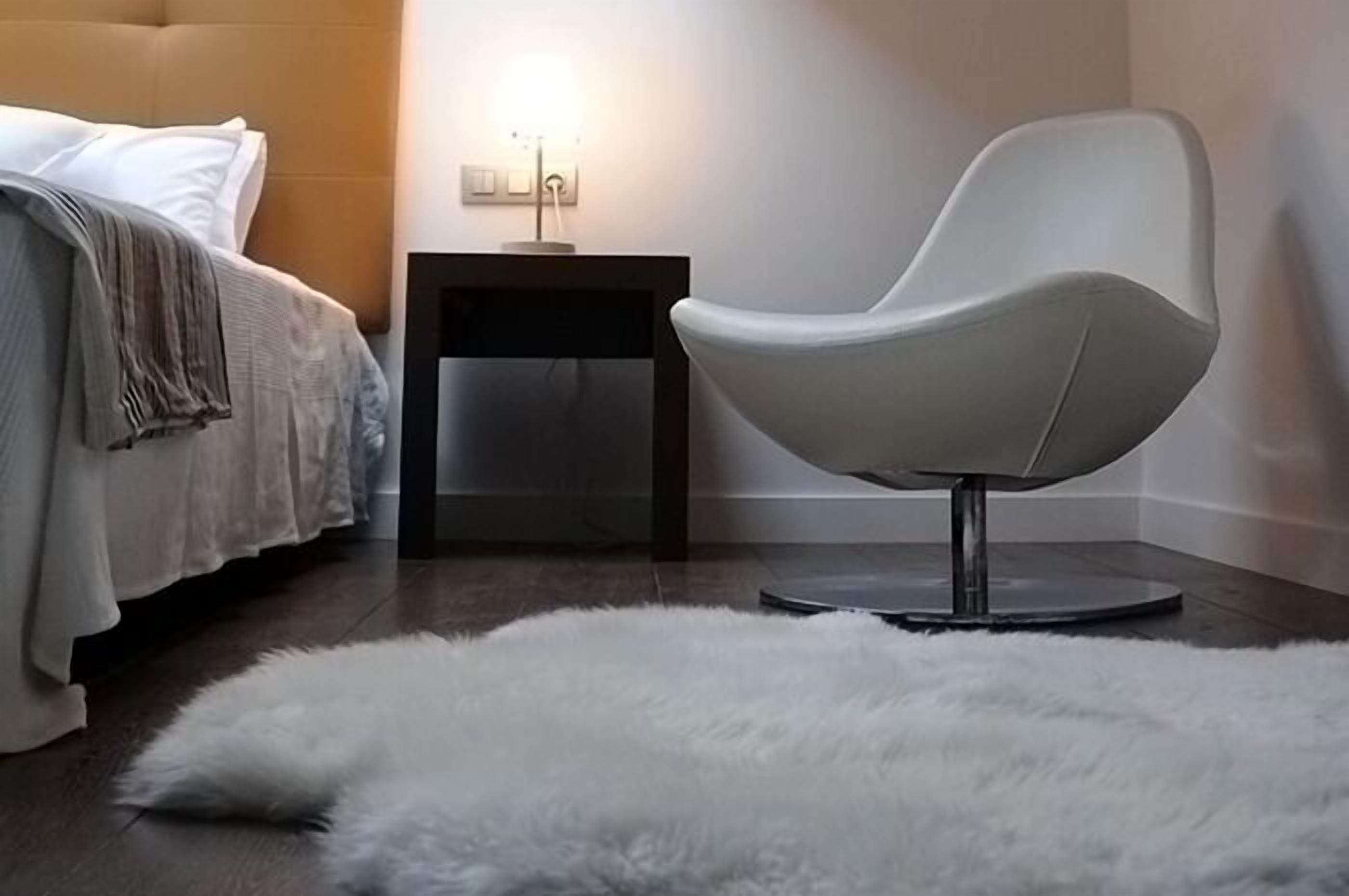 A modern bedroom with a bed, a white chair, a small table, and a fluffy rug.