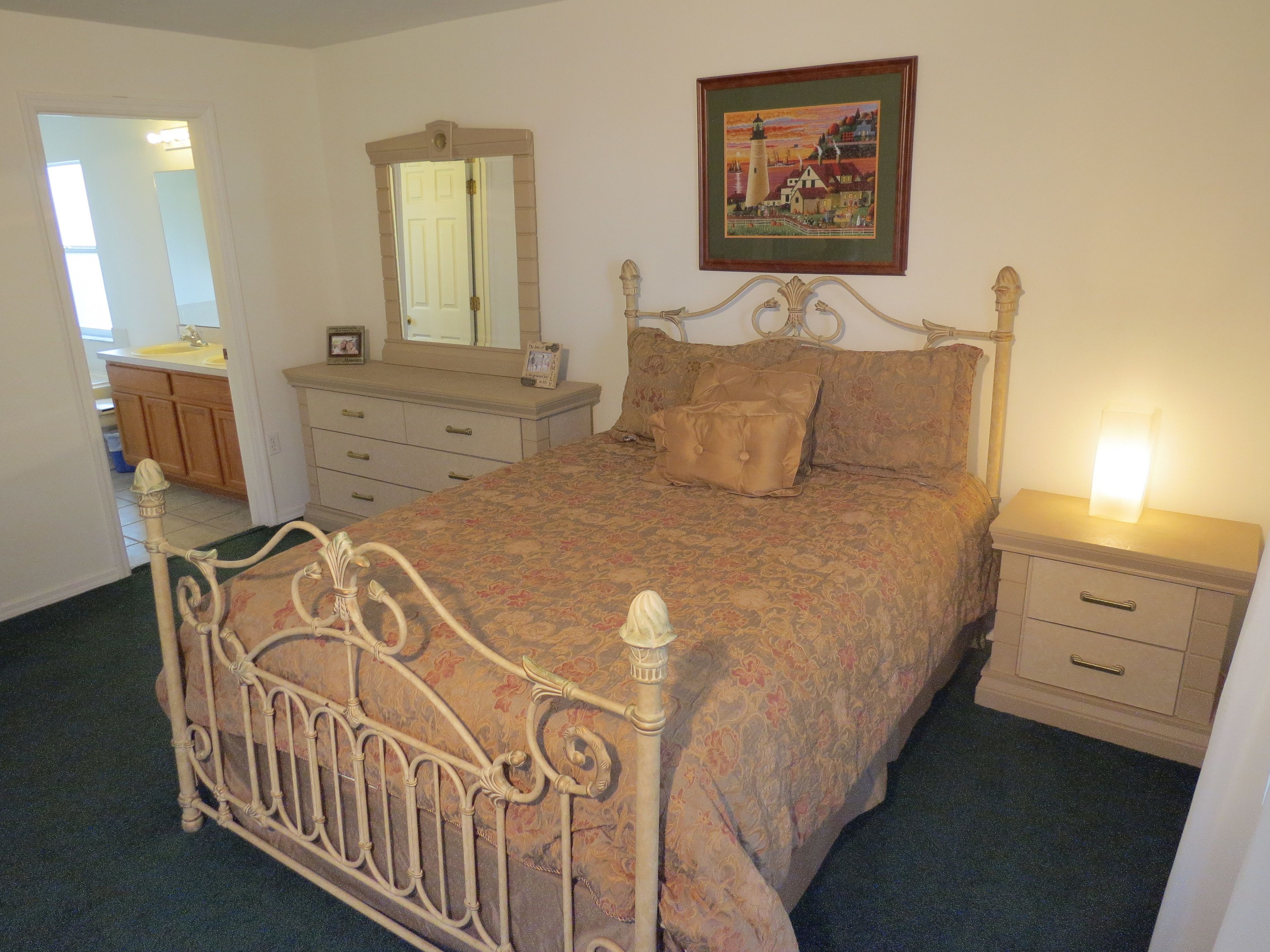 A bedroom with a bed, dresser, mirror, and bedside table.