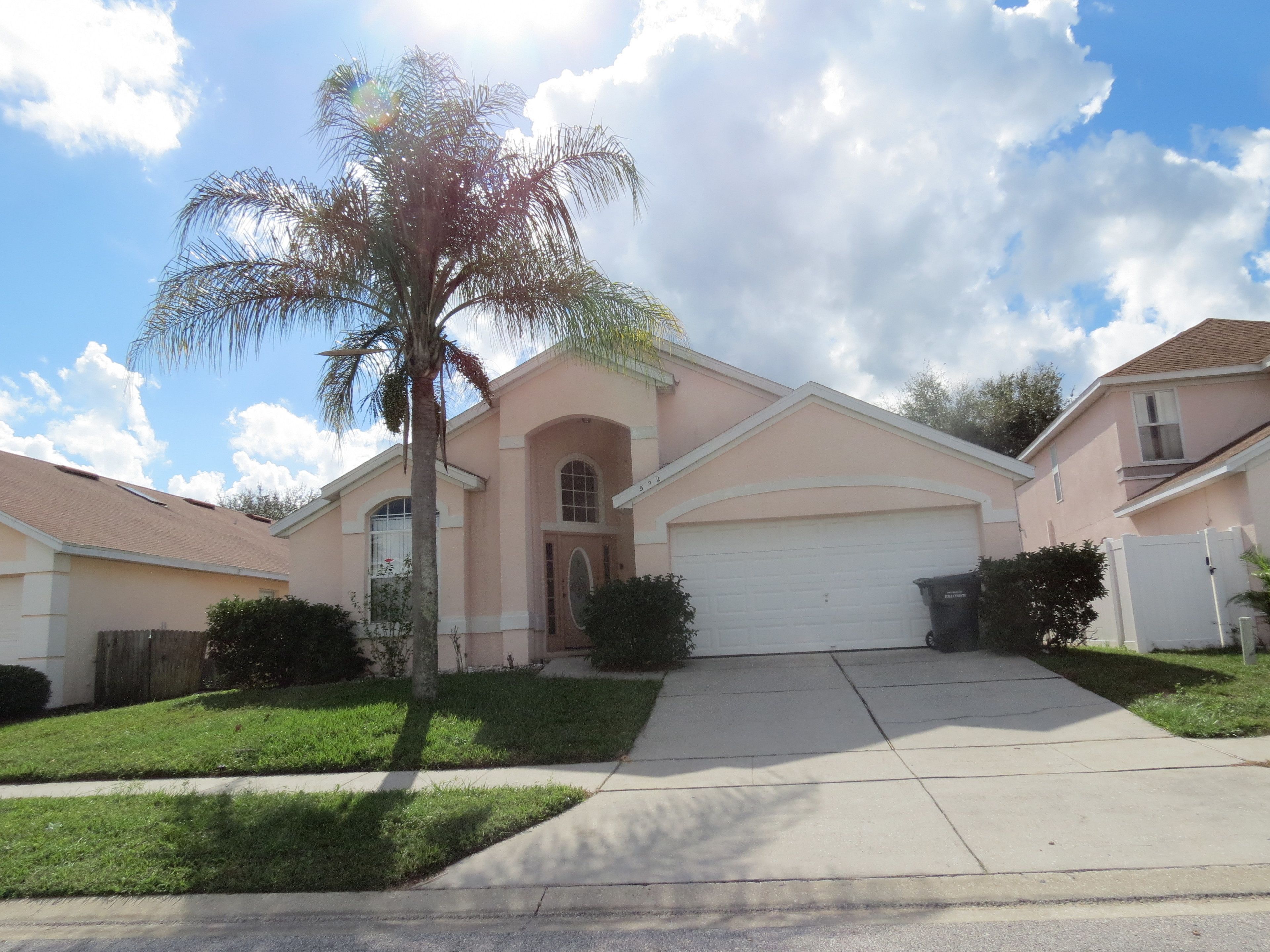 Una casa suburbana con un garaje individual, un césped cuidado y una palmera.