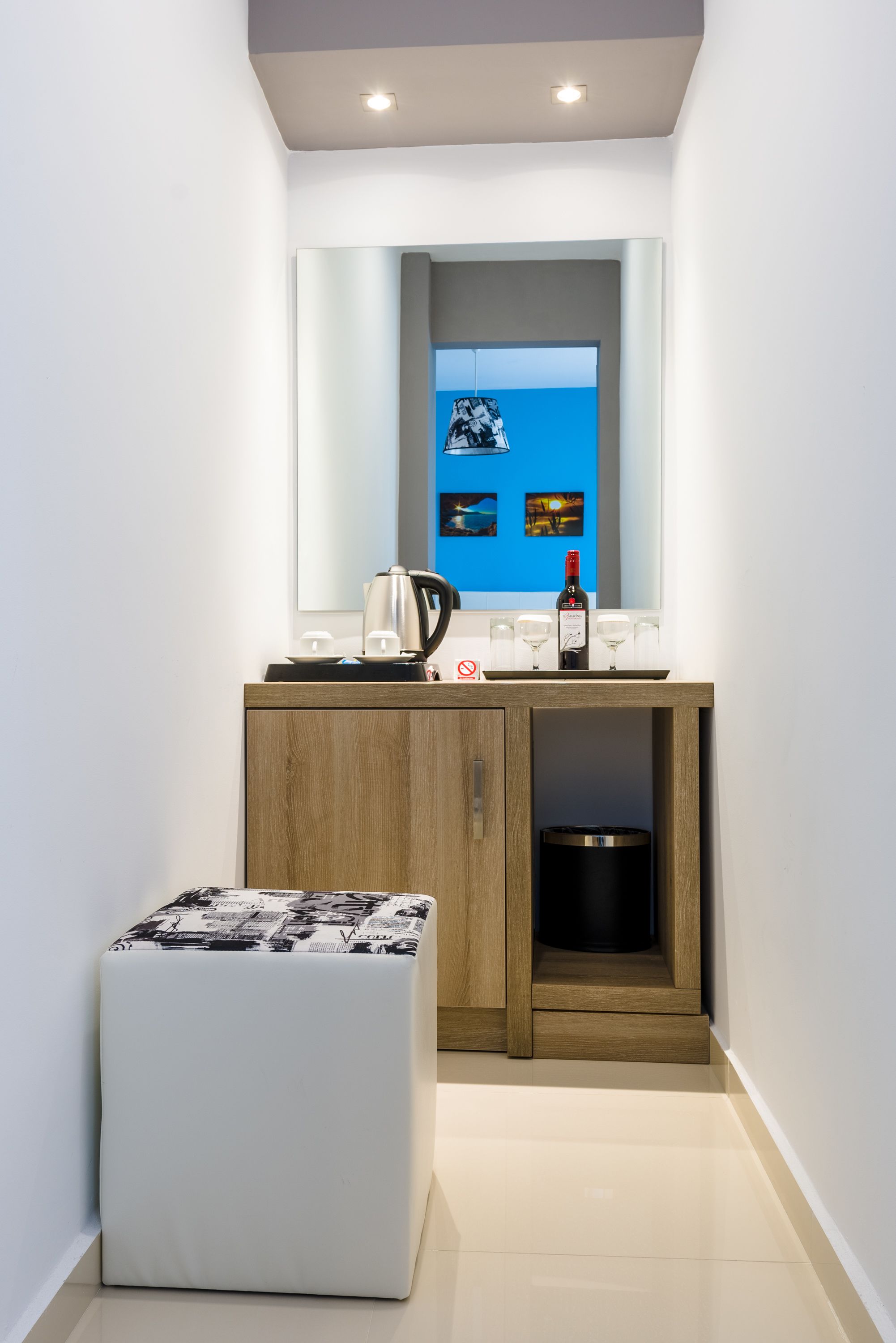 A modern bathroom with a wooden vanity, a mirror, a sink, a kettle, wine glasses, and a trash bin.