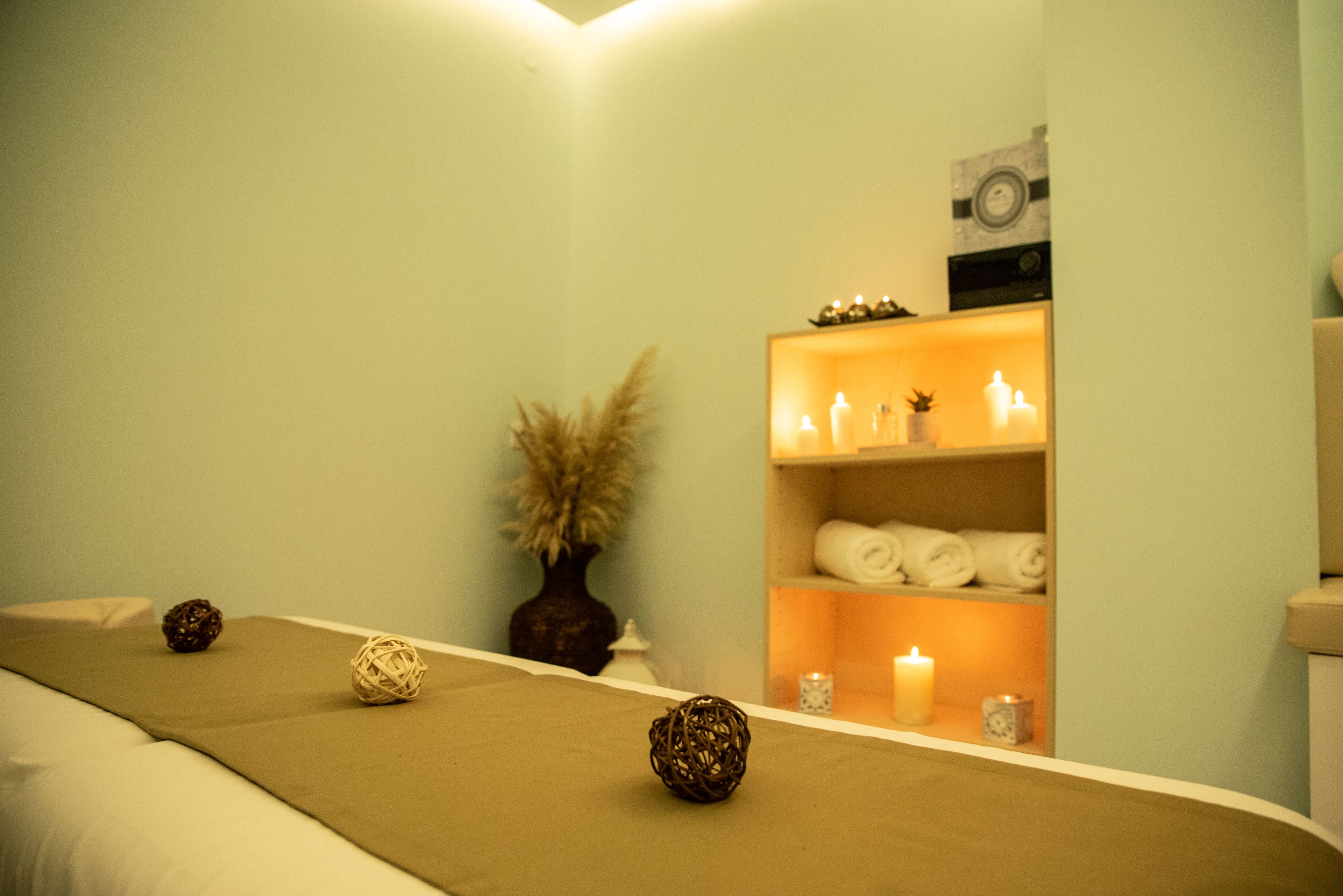 A spa room with a massage table, candles, and a shelf with towels and a clock.