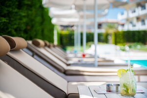 Zona de descanso junto a la piscina, con una bebida en un tarro de vidrio, un cenicero metálico y un menú sobre la mesa.