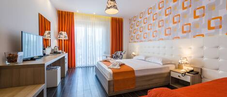 Una habitación de hotel moderna con cama, mesita de noche, lámpara y televisor sobre un escritorio.