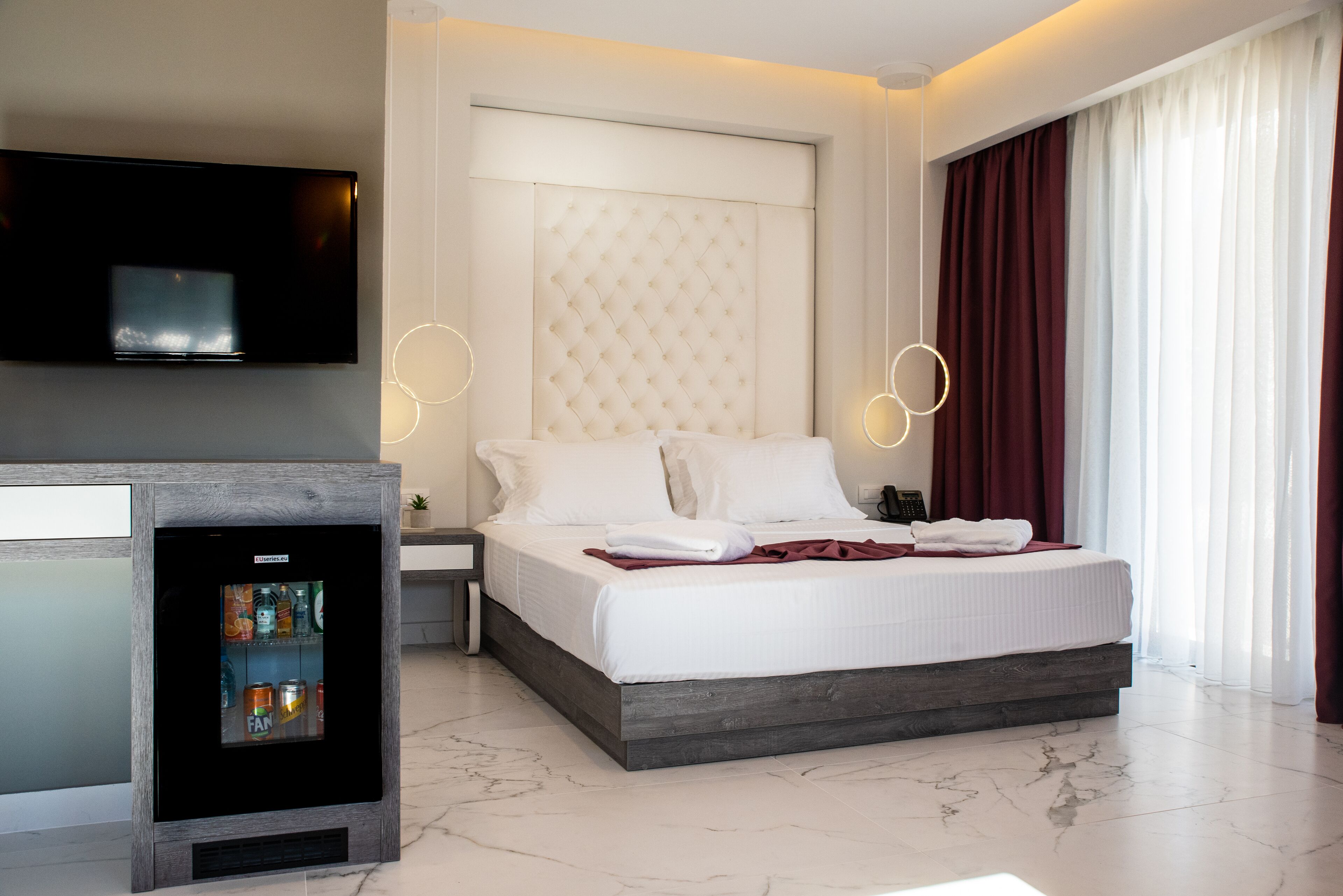 Una habitación de hotel moderna con una cama grande, un televisor de pantalla plana en la pared y un minibar.