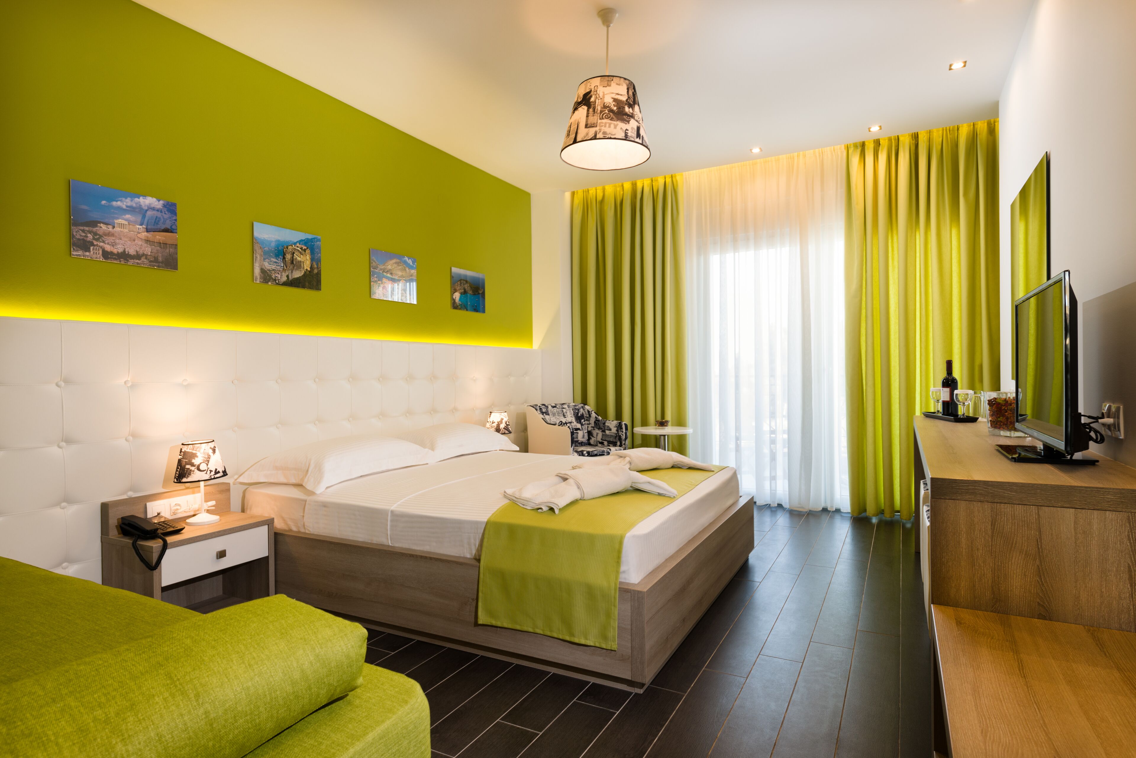 A modern hotel room with a large bed, a bedside table with a lamp, a TV, and a wooden desk.