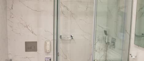 Un baño moderno con ducha de vidrio, lavamanos blanco y suelo de mármol.