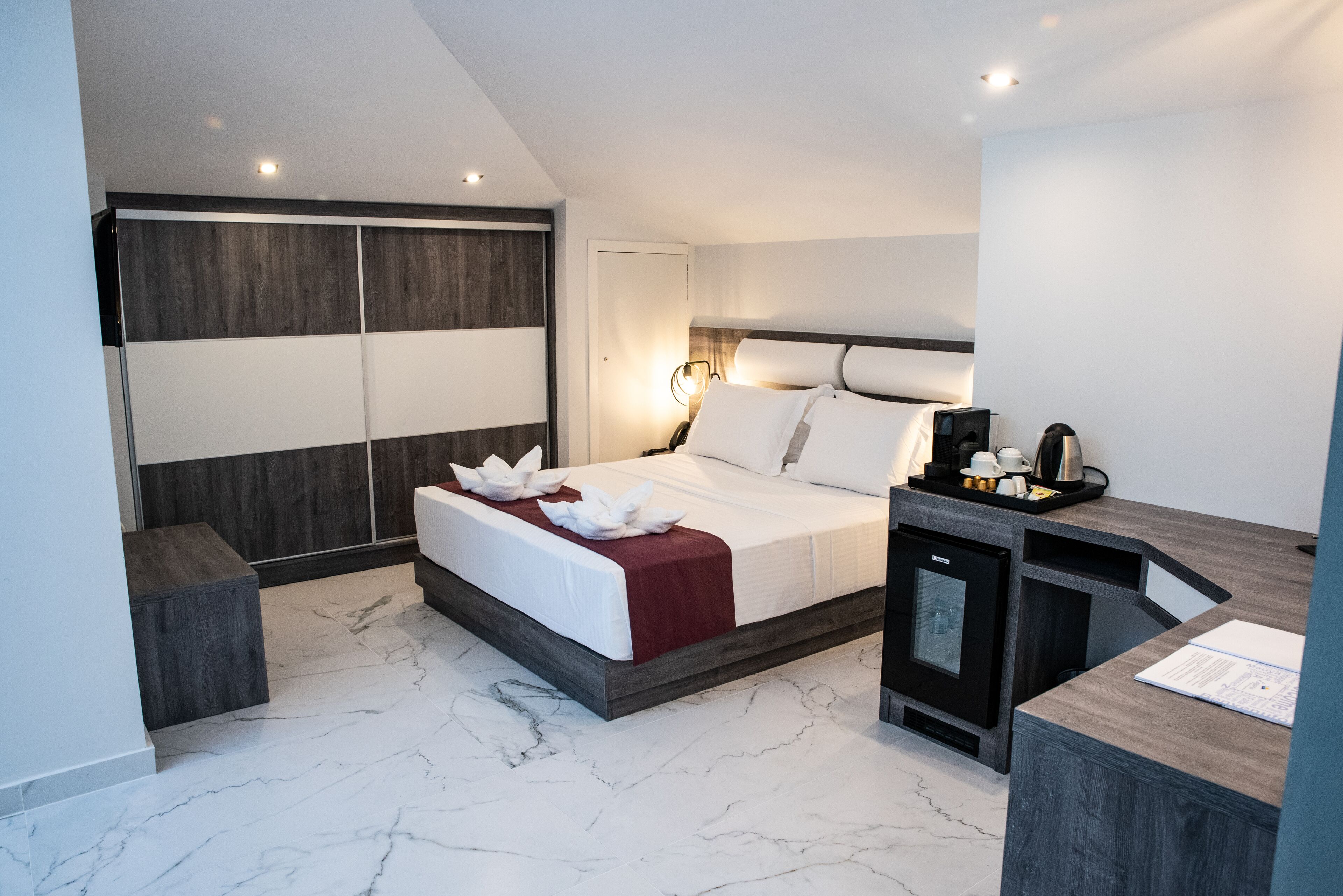 A modern hotel room with a large bed, a desk, and a minibar.