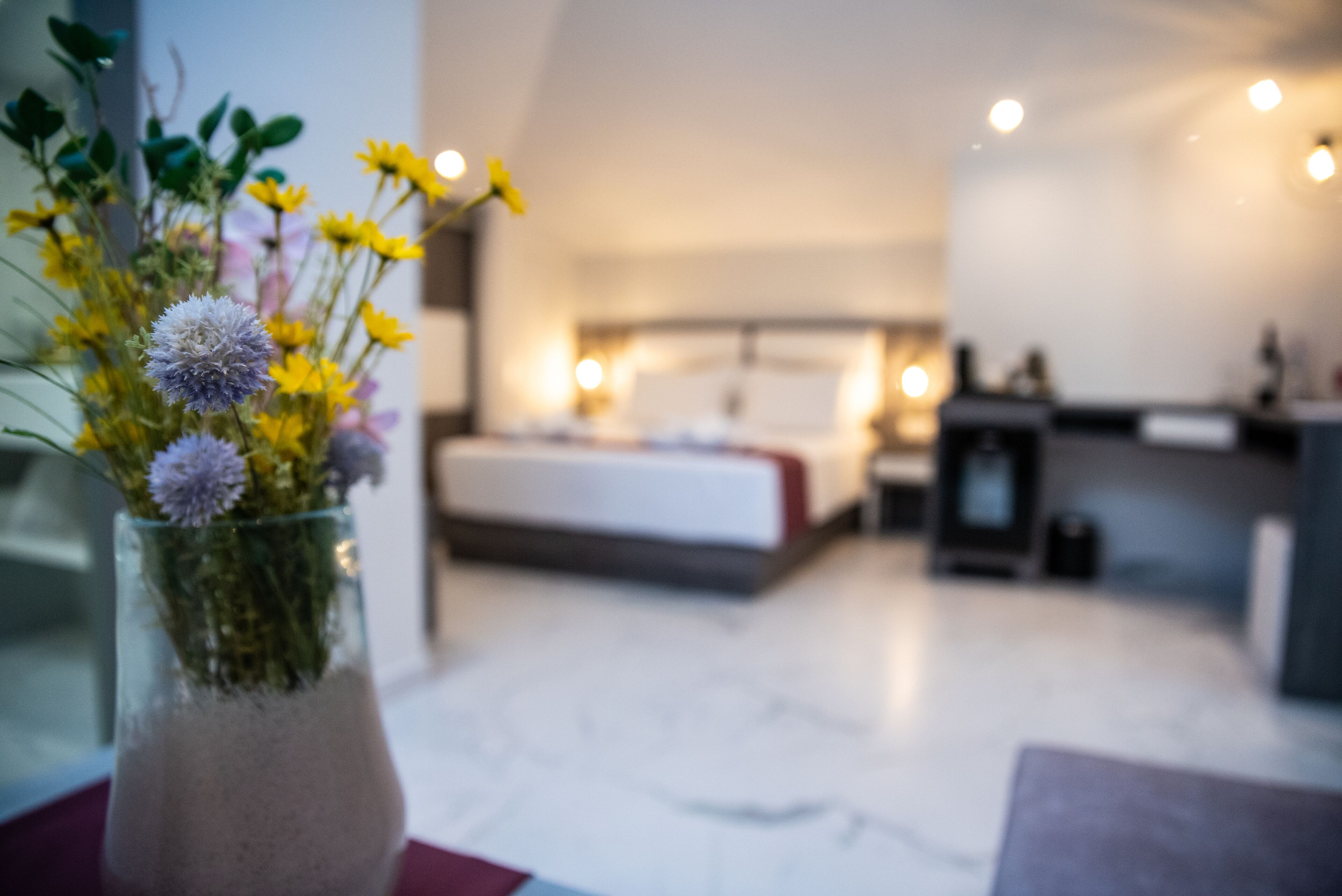 Una habitación de hotel moderna con una cama, una mesita de noche y un florero sobre una mesa.