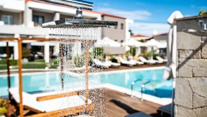 A modern outdoor pool area with a water feature, lounge chairs, and a clear blue sky. - Lagaria Hotel (Kassandra)