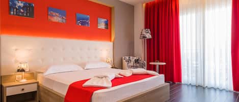 A modern hotel room with a large bed, red curtains, and artwork on the wall.