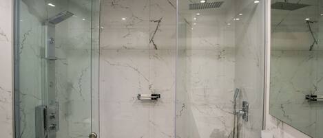 A modern bathroom with a glass-enclosed shower, marble walls, and a white sink with toiletries.