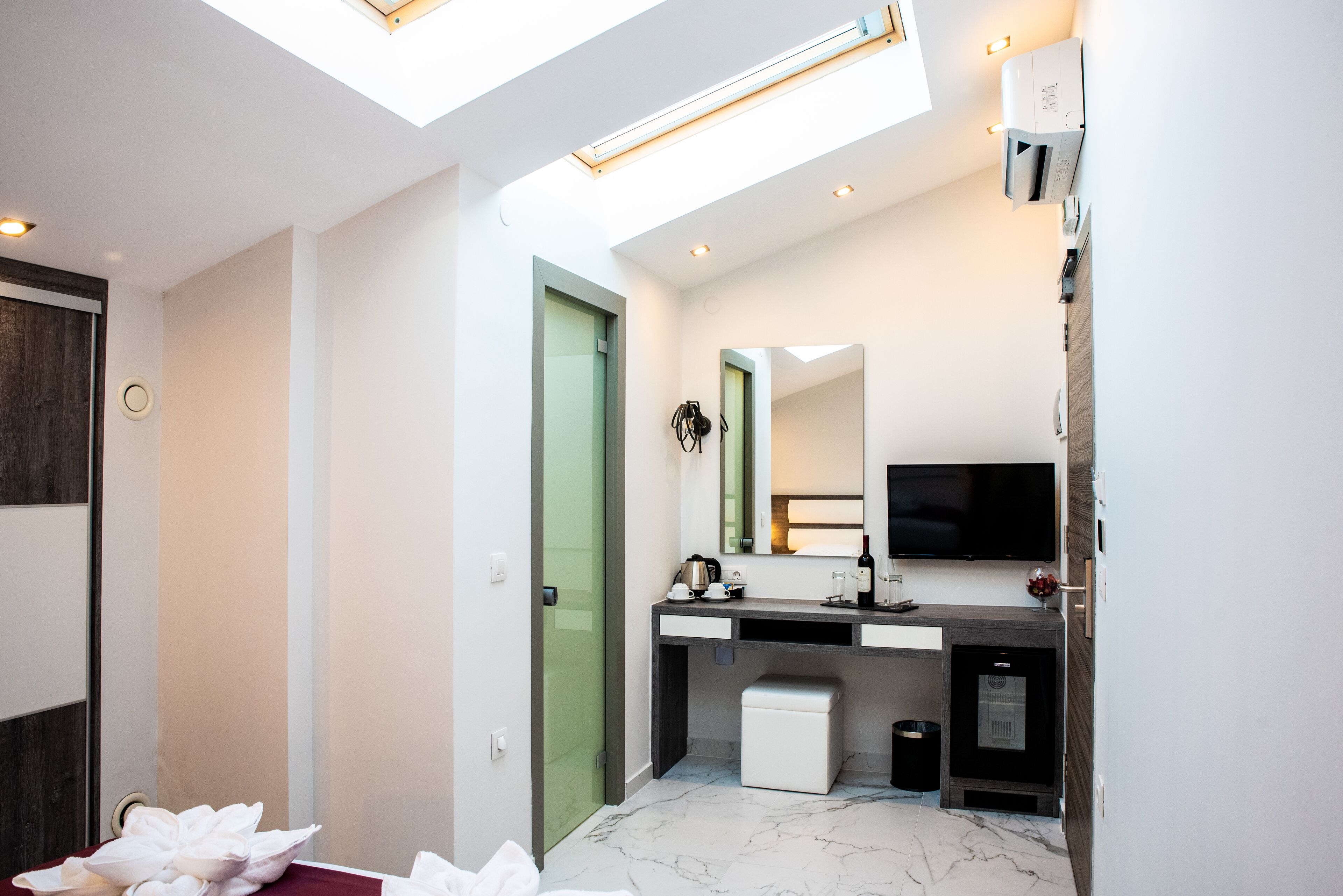 A modern bathroom with a skylight, a large mirror, a television, and a small trash bin.
