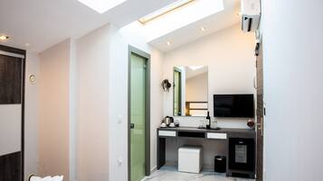 A modern bathroom with a skylight, a large mirror, a television, and a small trash bin.