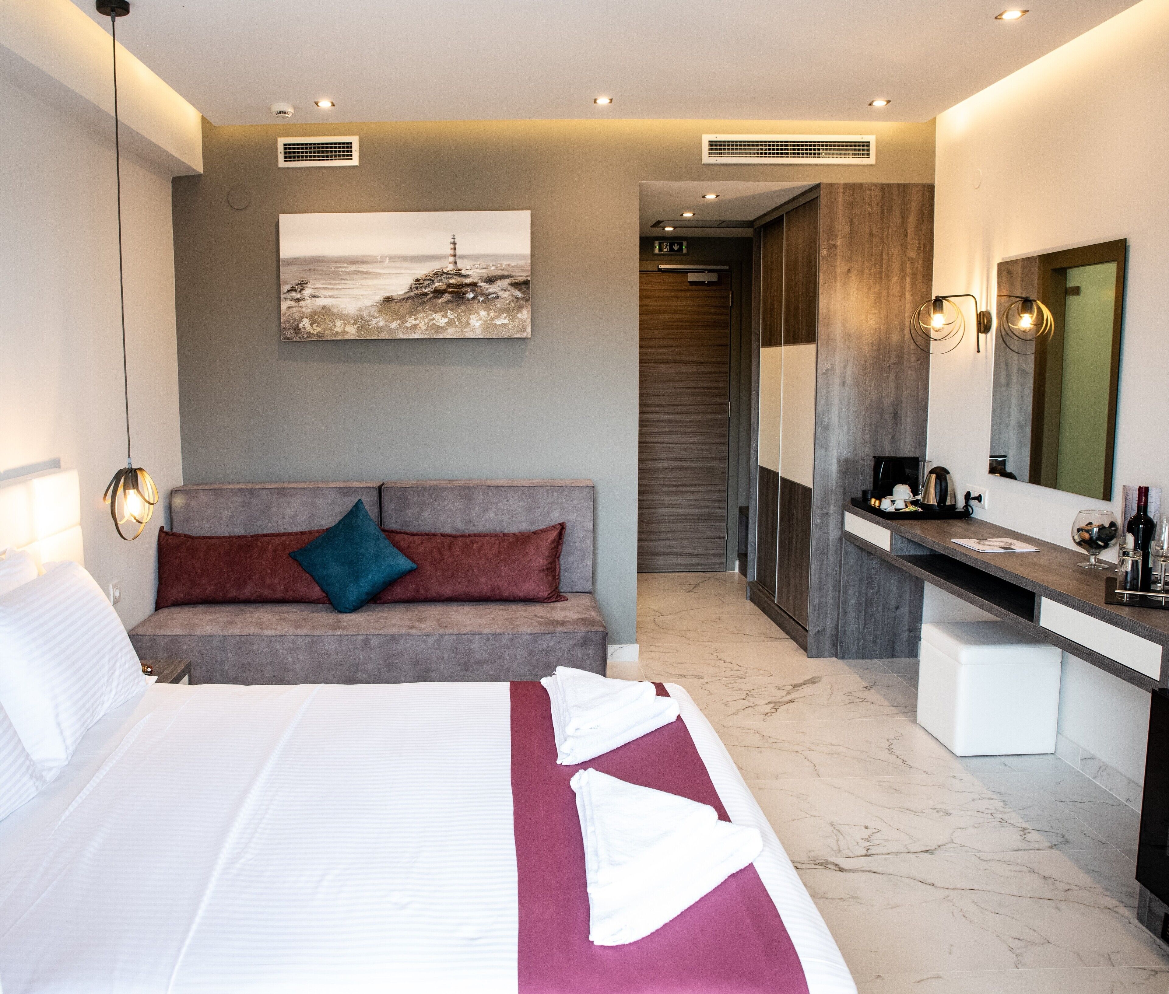 Een moderne hotelkamer met een groot bed, een slaapbank, een kaptafel met spiegel en een schilderij aan de muur.