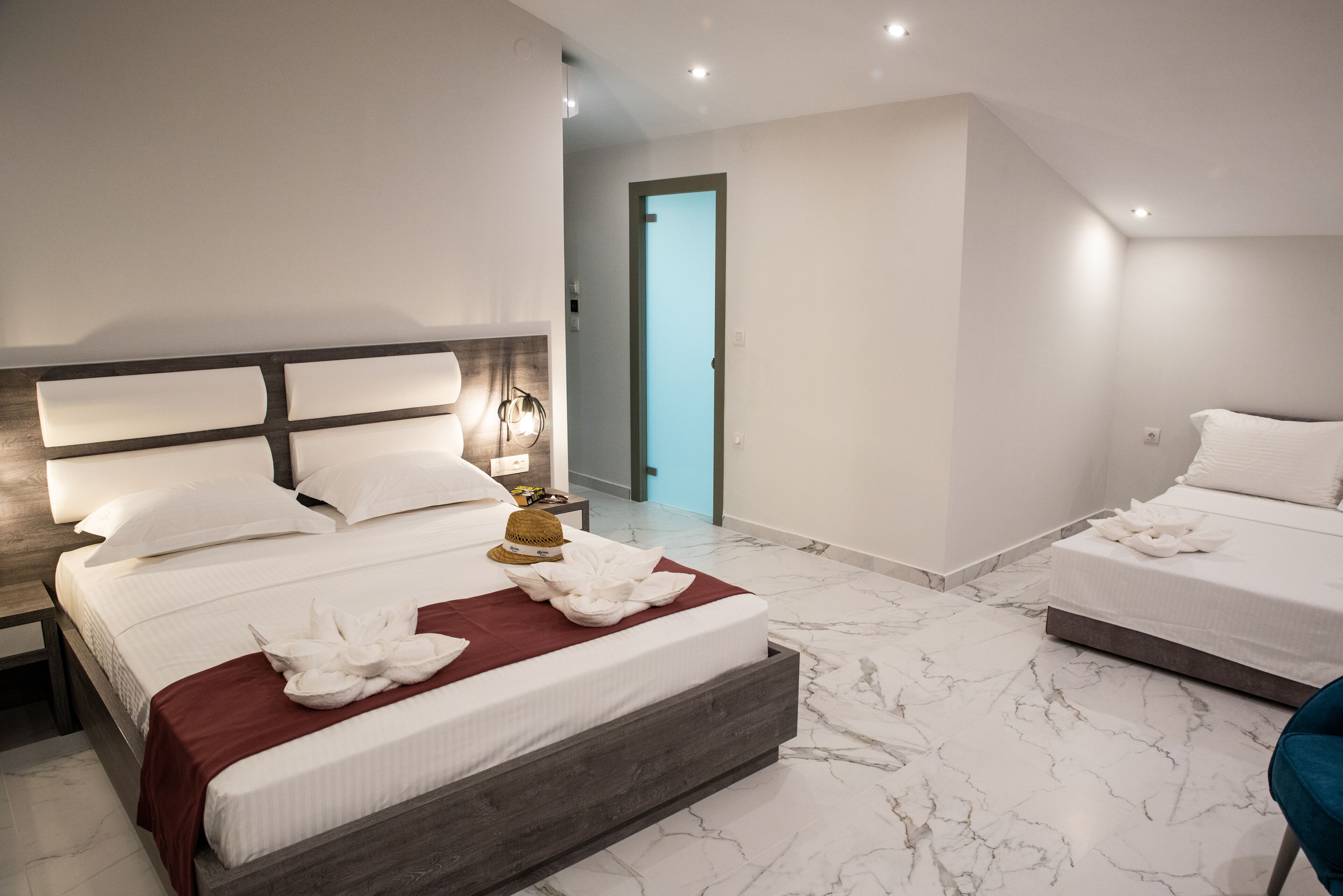 A modern hotel room with a large bed, a smaller bed, and a bathroom visible through an open door.