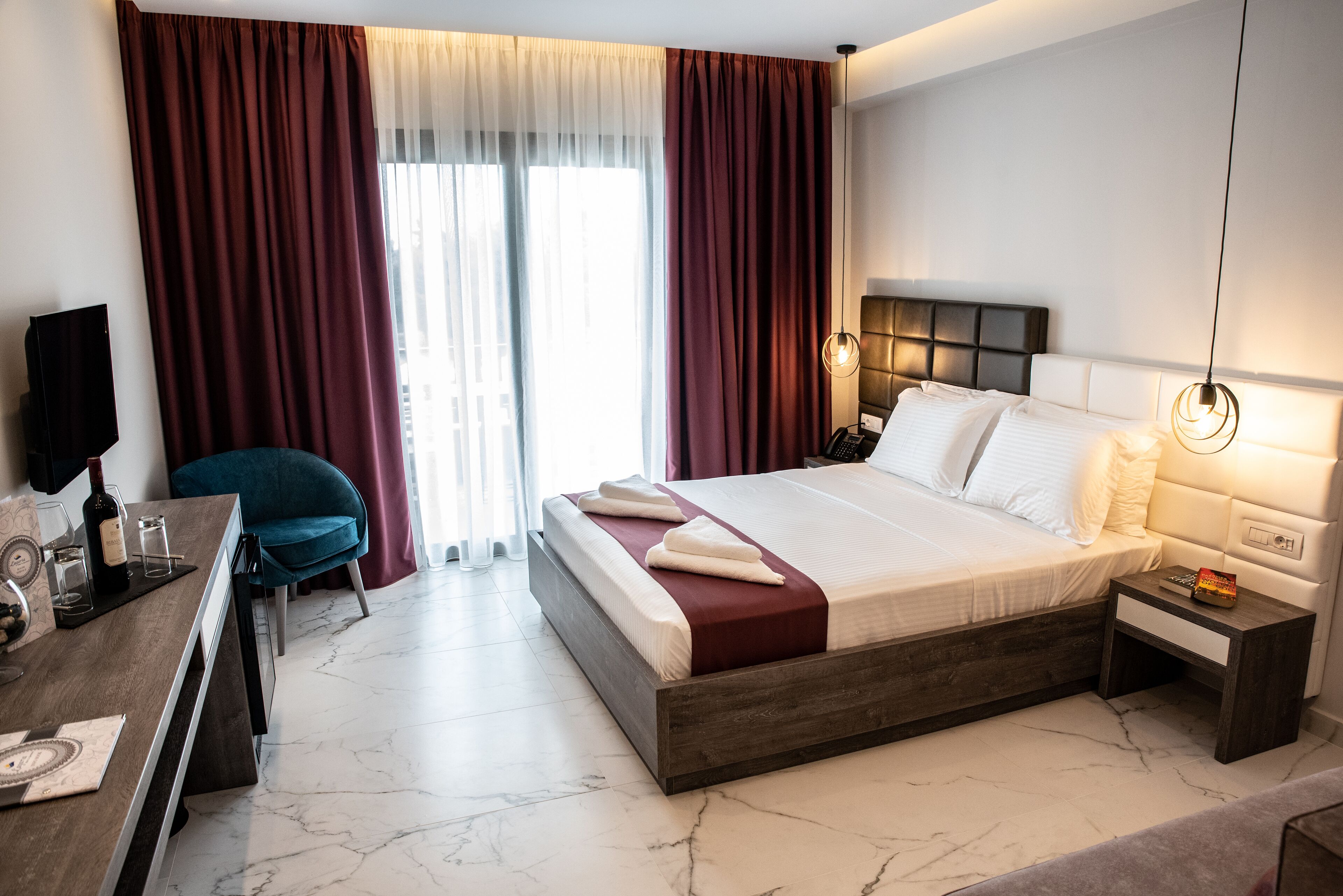Habitación de hotel con una cama grande, un escritorio con silla, un televisor y una ventana con cortinas.