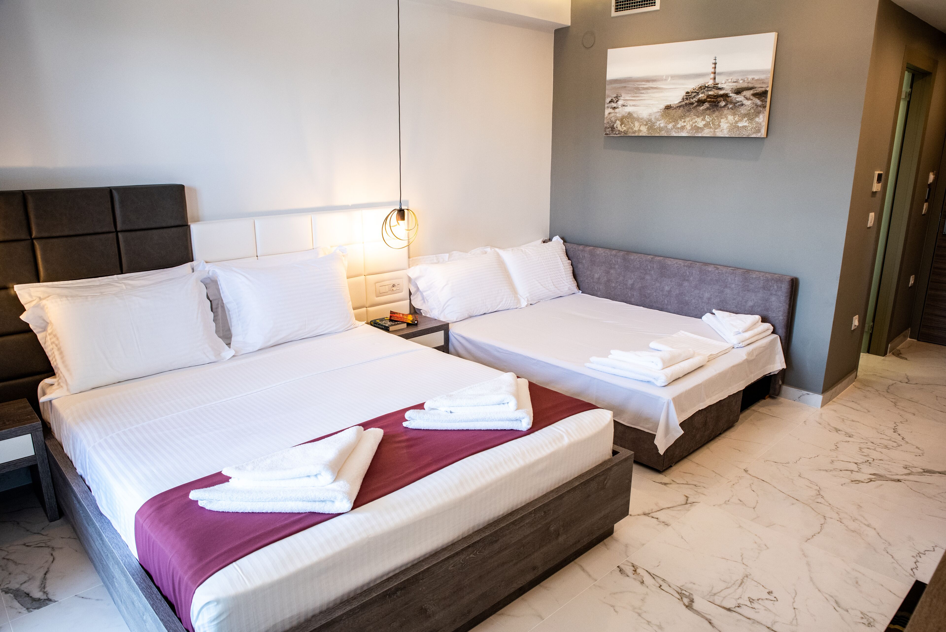 A hotel room with two beds, marble flooring, a painting on the wall, and a nightstand with a lamp.
