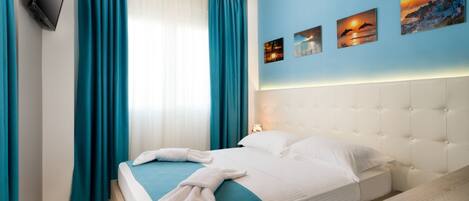 A hotel room with a bed, a bedside table, a flat-screen TV mounted on the wall, and a window with curtains.