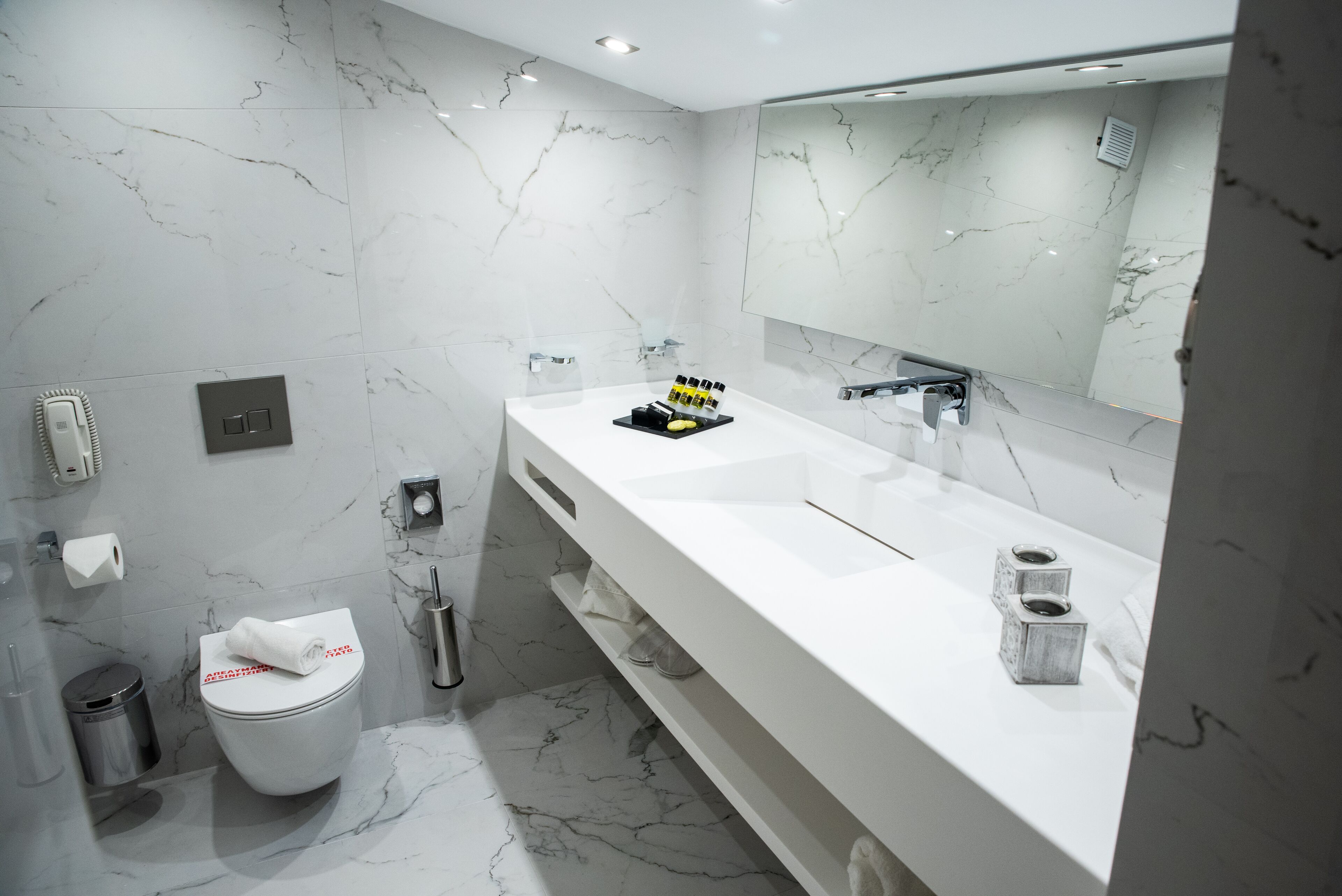 Et moderne badeværelse med en hvid marmorvask, et stort spejl og et toilet.