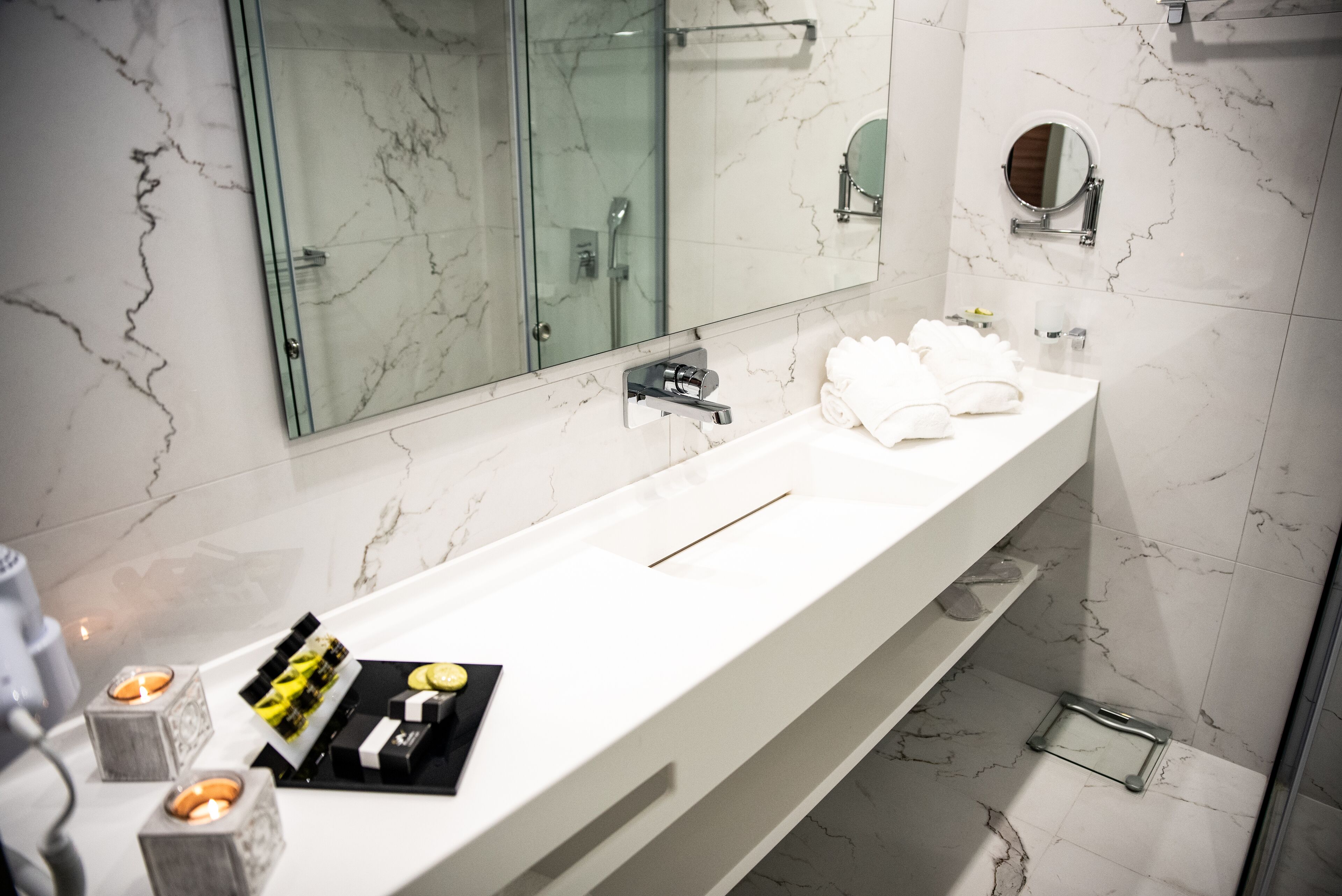 A modern bathroom with a long white sink, a glass shower enclosure, and a large mirror.