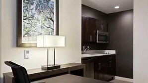 A modern kitchen with dark cabinets, a stainless steel microwave, and a window with a tree painting. - Hampton Inn & Suites Richmond - Downtown (Richmond)