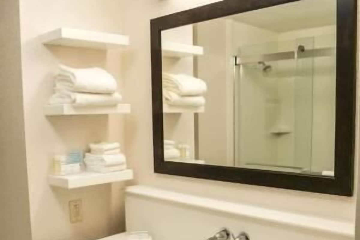 Un baño con un lavamanos blanco, un espejo y estantes con toallas dobladas.