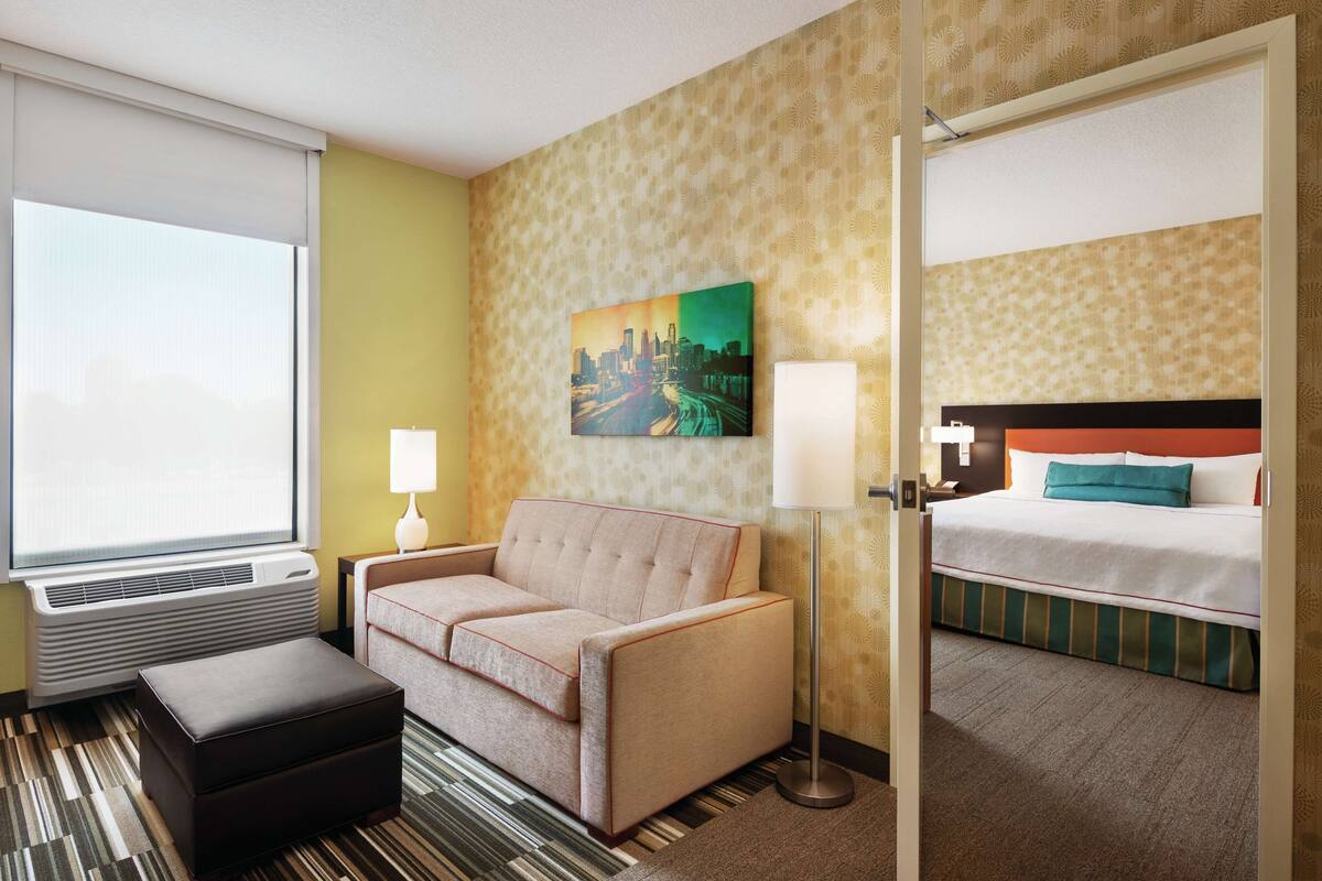 Une chambre d’hôtel avec un canapé, un lit, une lampe et un tableau représentant un paysage urbain.