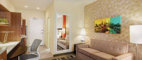 A hotel room with a desk, office chair, sofa, and a cityscape painting on the wall.