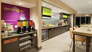 Een modern koffiehuis met een koffiehoek, afvalbakken en een zithoek met tafels en stoelen.