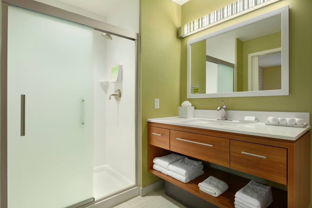 Une salle de bain moderne avec une douche à l’italienne en verre, un meuble-lavabo en bois avec un miroir et des serviettes soigneusement pliées.