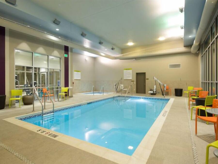 Una piscina interior con carriles claramente delimitados, zonas de estar cercanas con sillas, y una puerta visible que da a otra habitación.
