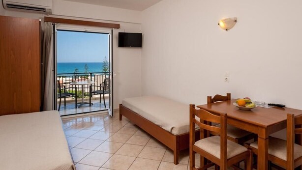 A room with a bed, a small table with chairs, a TV, and a balcony with a view of the sea. - Orion Star (Chania)