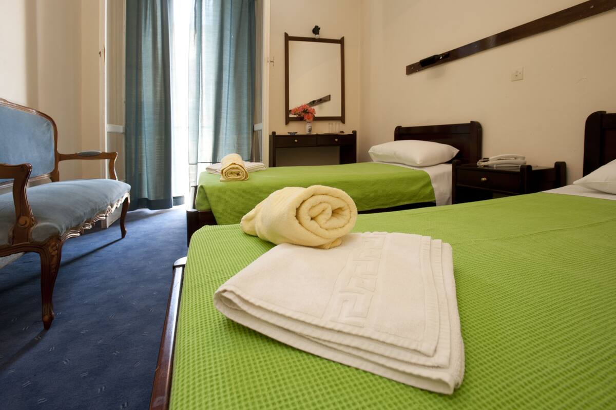 A hotel room with two beds, a wooden chair, a desk, and a mirror.