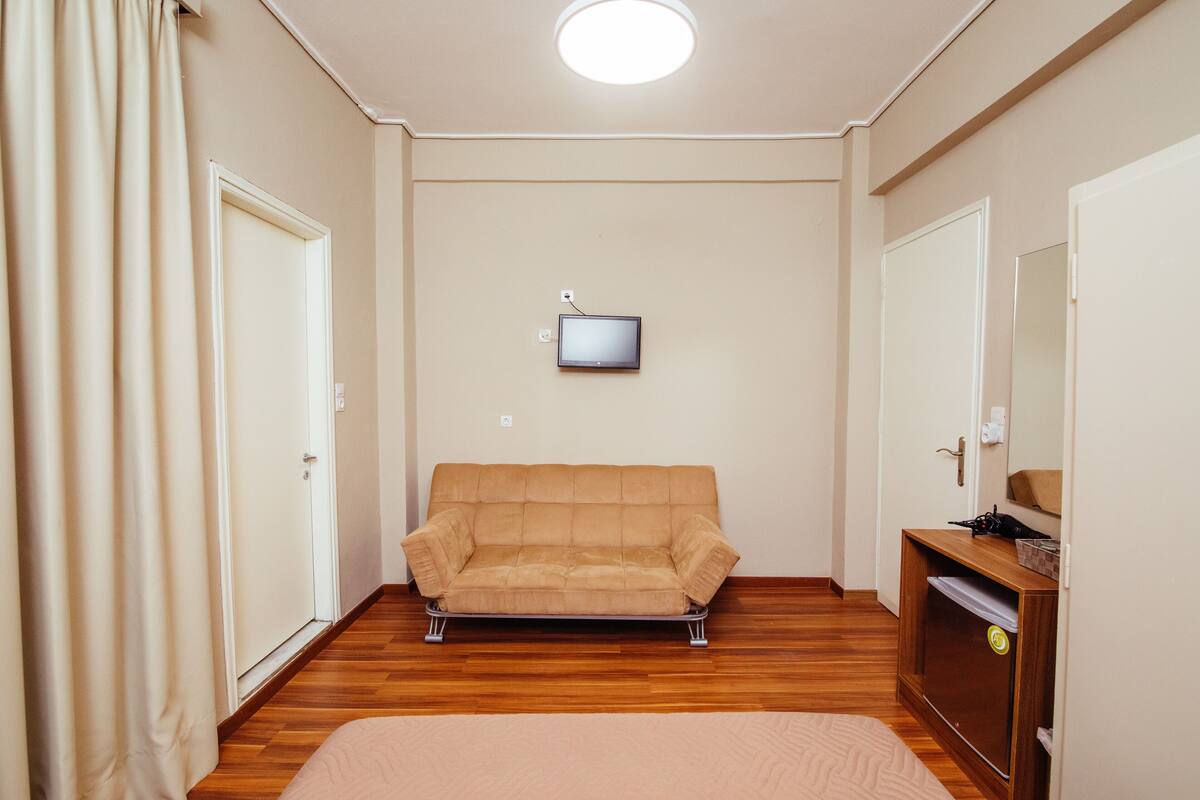 A room with a sofa, a television mounted on the wall, and a wooden cabinet.