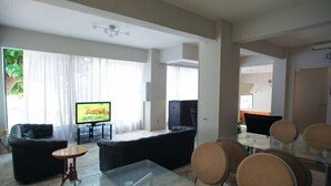 Una sala moderna con televisor de pantalla plana, asientos cómodos, una mesa de centro de vidrio y un comedor con sillas.