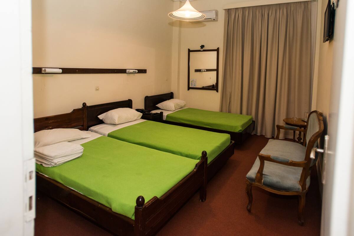 A hotel room with two single beds, a wooden chair, a small table, a mirror, and a hanging light fixture.