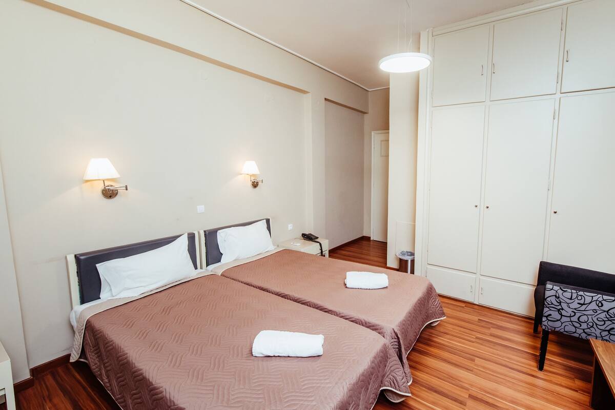A hotel room with two beds, a wardrobe, a desk, and a bench.