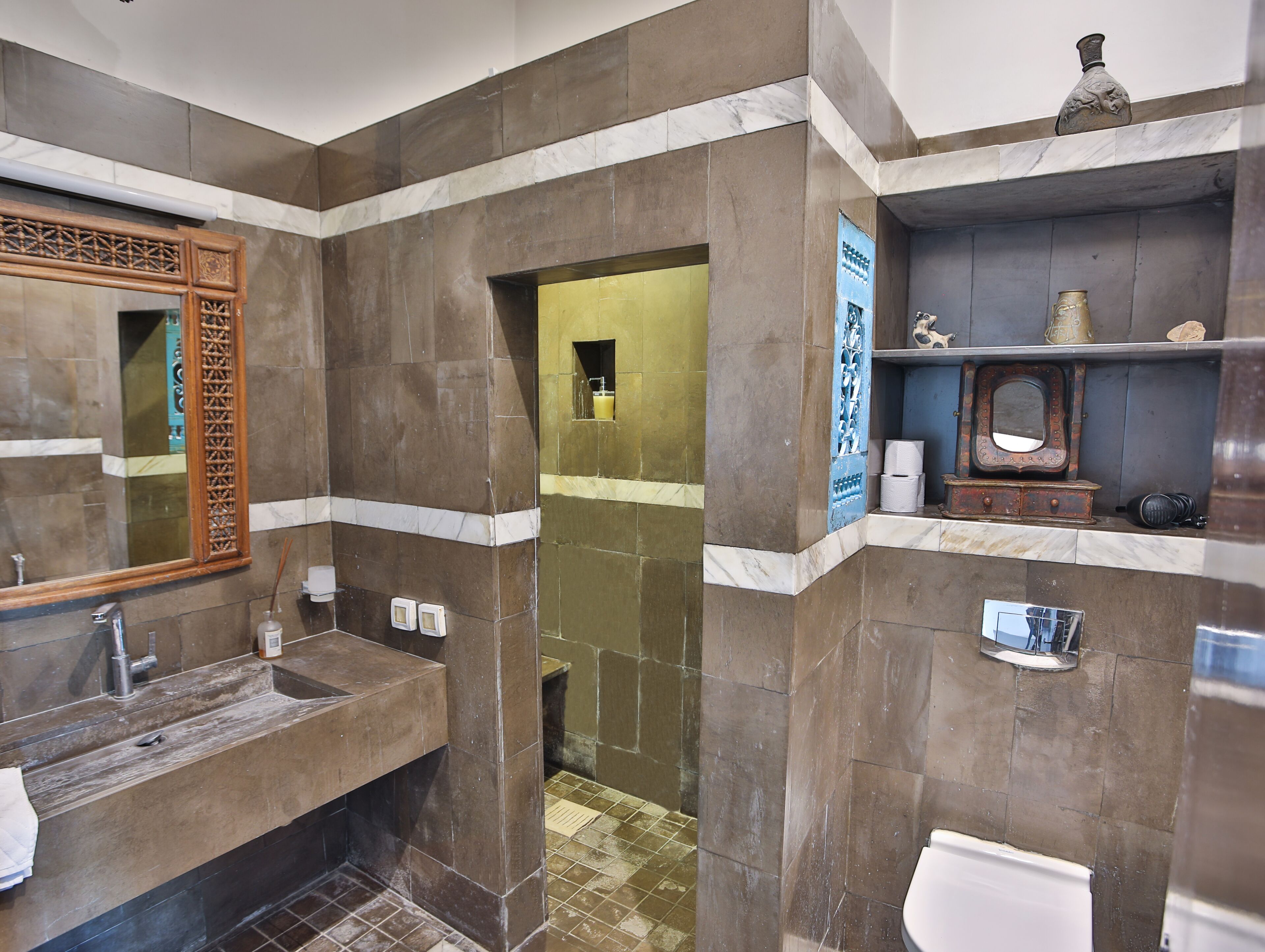 A bathroom with a sink, mirror, and toilet. There is a decorative mirror frame and a shelf with toiletries.