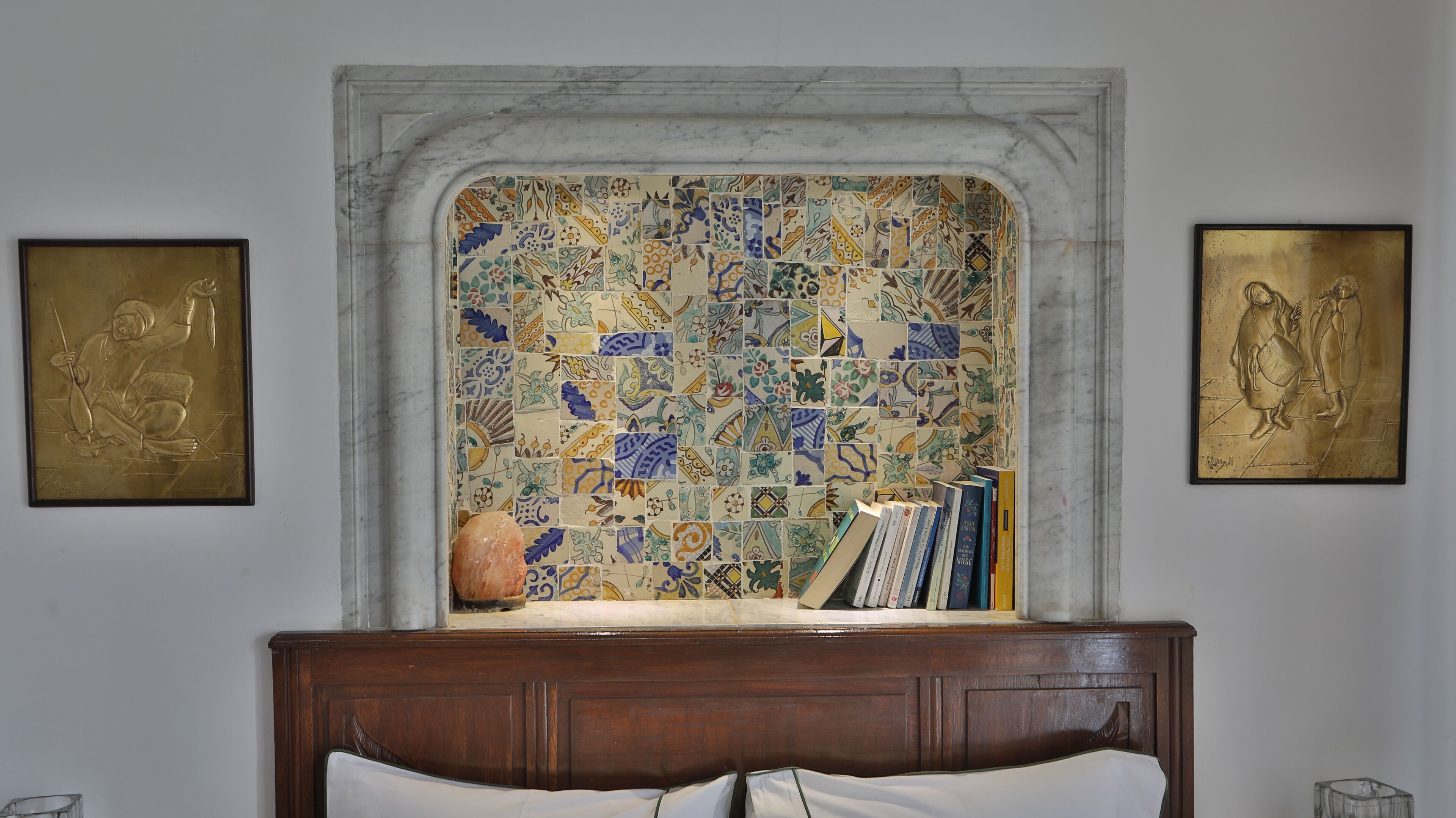 Een slaapkamer met een marmeren open haard, een bed en twee ingelijste kunstwerken aan de muur.