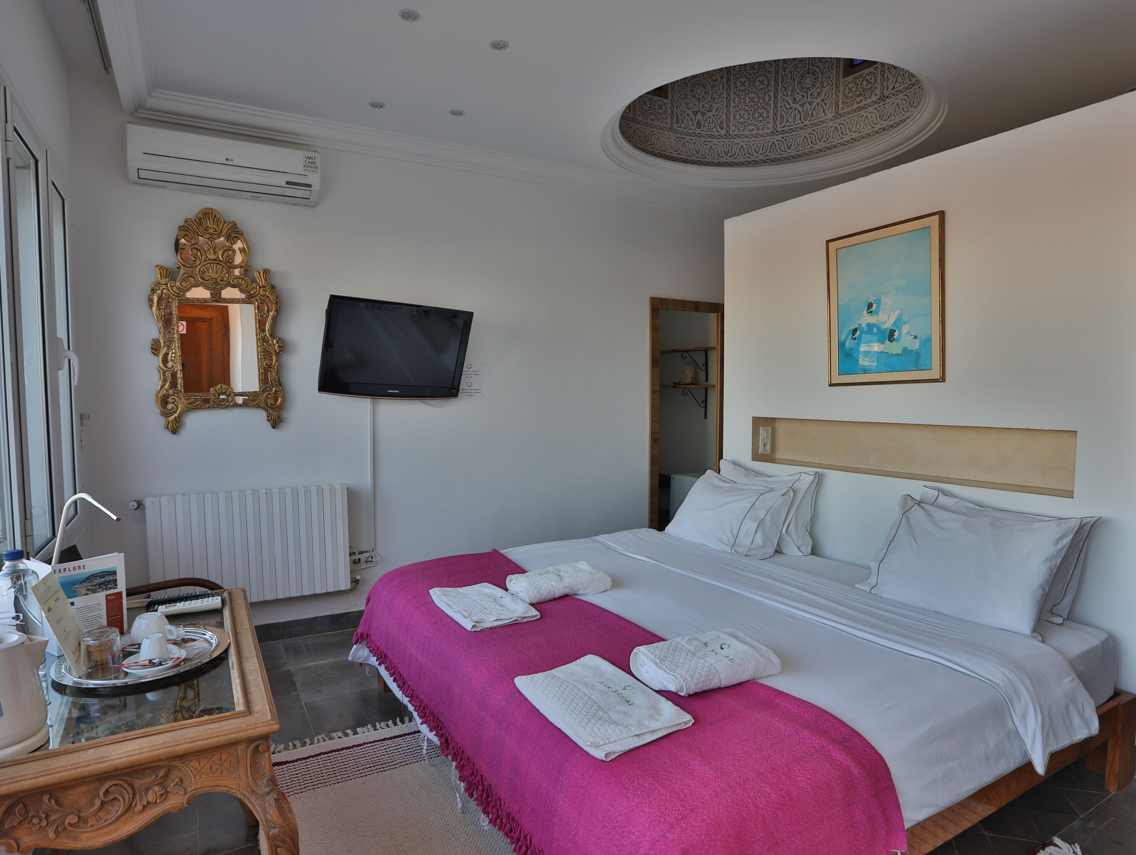 A hotel room with a bed, a TV, a mirror, and a painting on the wall.