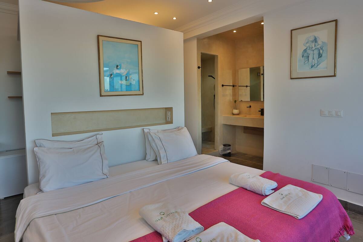 Una habitación de hotel con una cama grande, un baño con espejo y un cuadro en la pared.