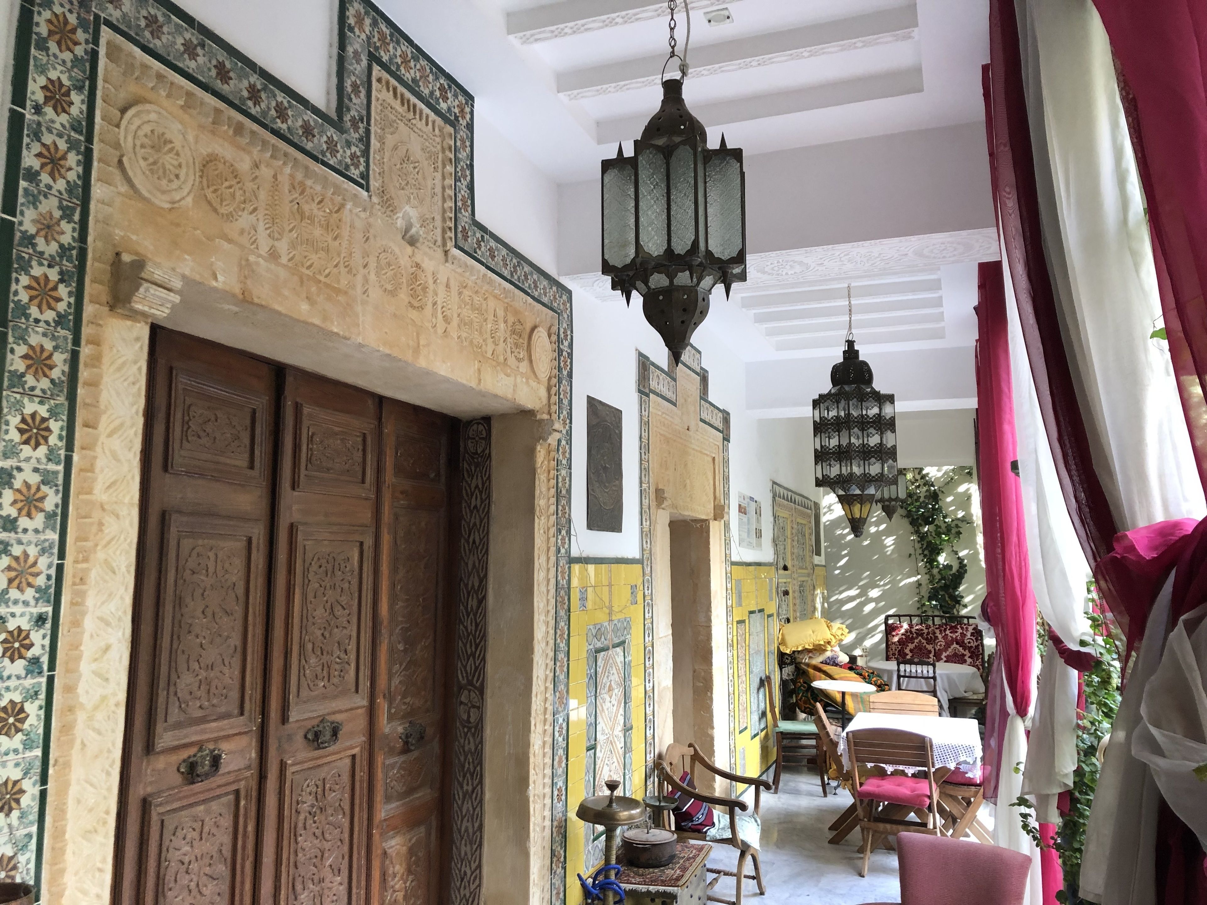 A traditional interior with ornate wooden doors, patterned tile walls, and hanging lanterns.