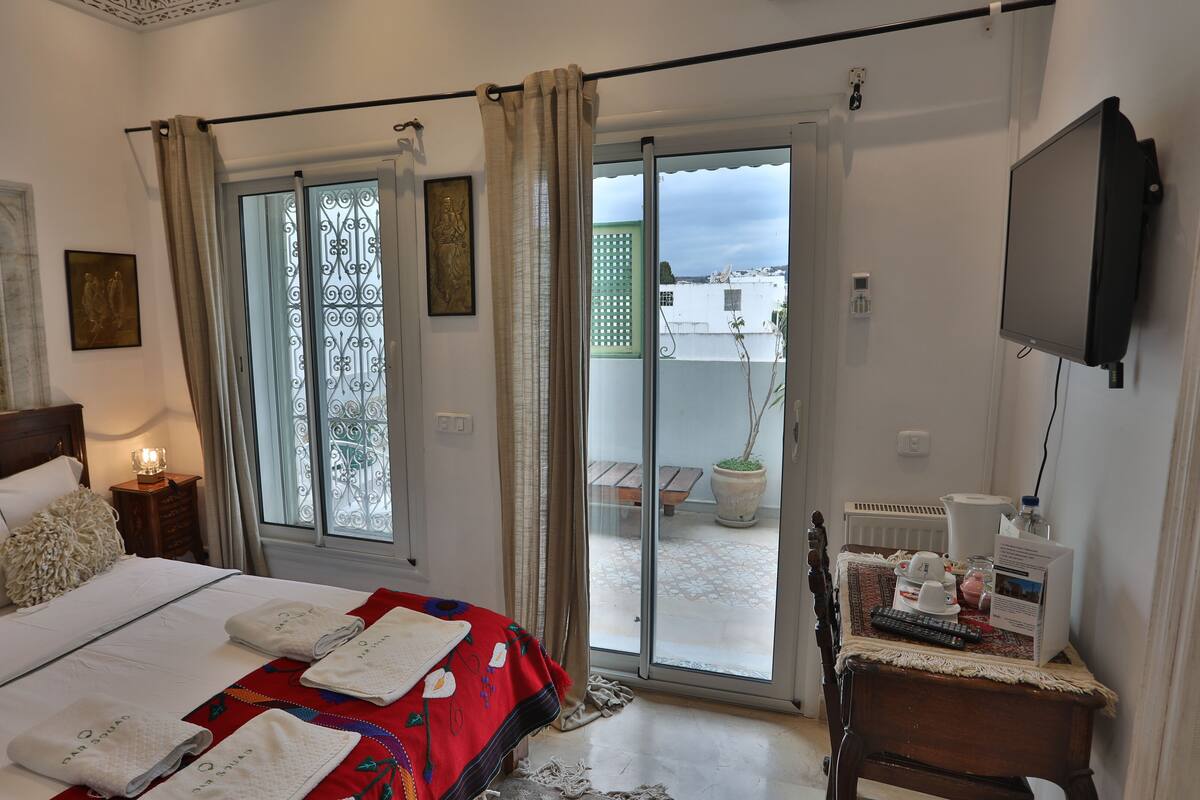 Habitación de hotel con una cama, televisión, una mesita con un control remoto y vistas al balcón exterior.