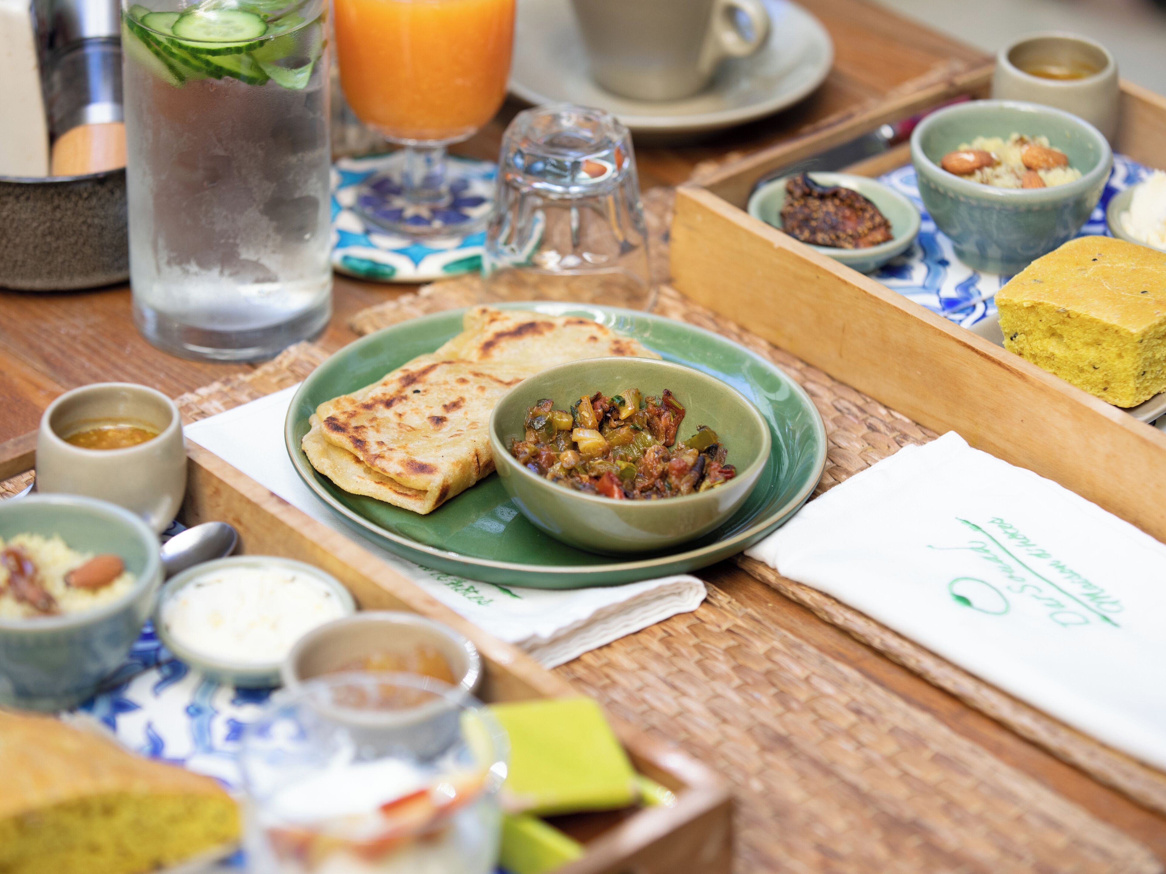 A breakfast setting with various dishes, including flatbreads, a bowl of mixed vegetables, and multiple small bowls of dips.